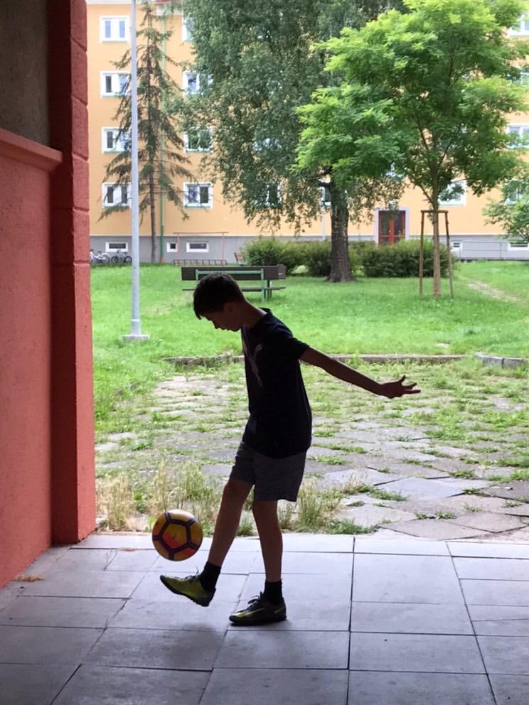 A boy in silhouette keeps a ball in the air near a block of flats